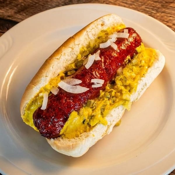 A hot dog in a bun with mustard, relish, and chopped onions on a white plate.