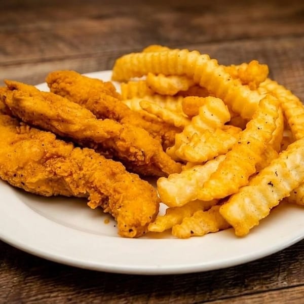 Crispy golden chicken tenders and crinkle-cut fries on a white plate, on a rustic wooden table.