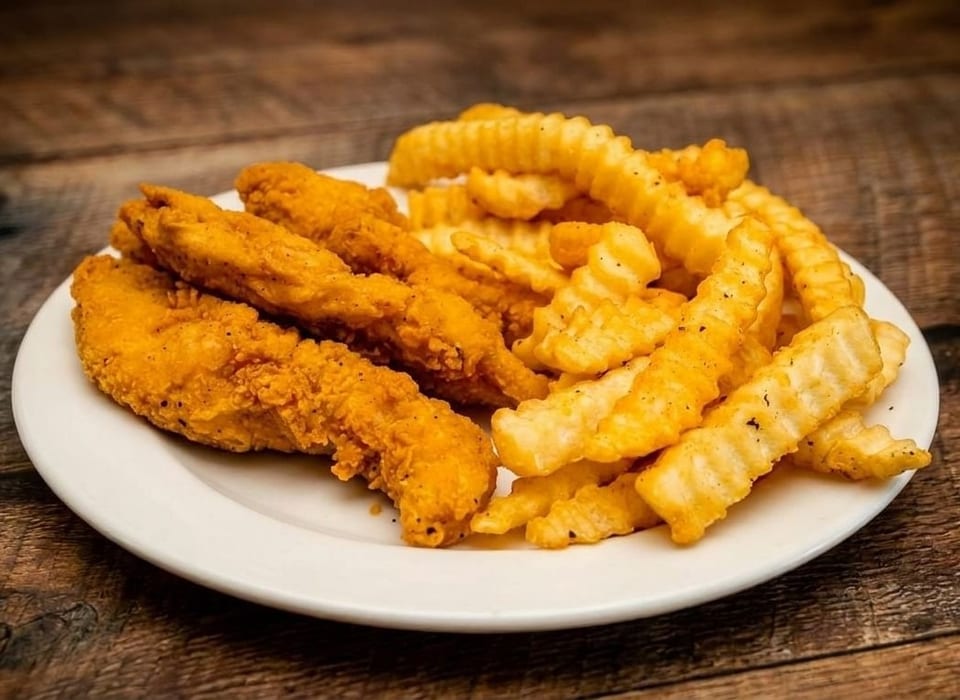 Crispy golden chicken tenders and crinkle-cut fries on a white plate, on a rustic wooden table.