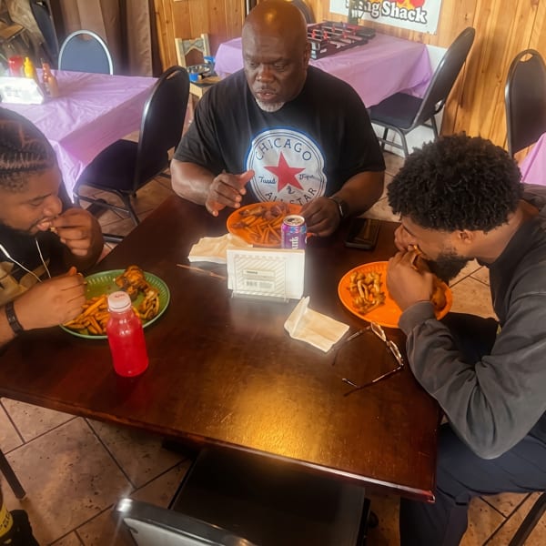 Three men enjoying plates of chicken wings and fries at a restaurant table.